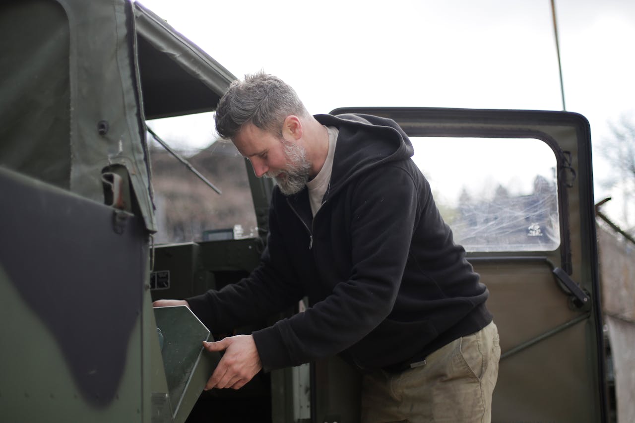 A mechanic focuses on inspecting a military vehicle outdoors, exuding professional expertise.